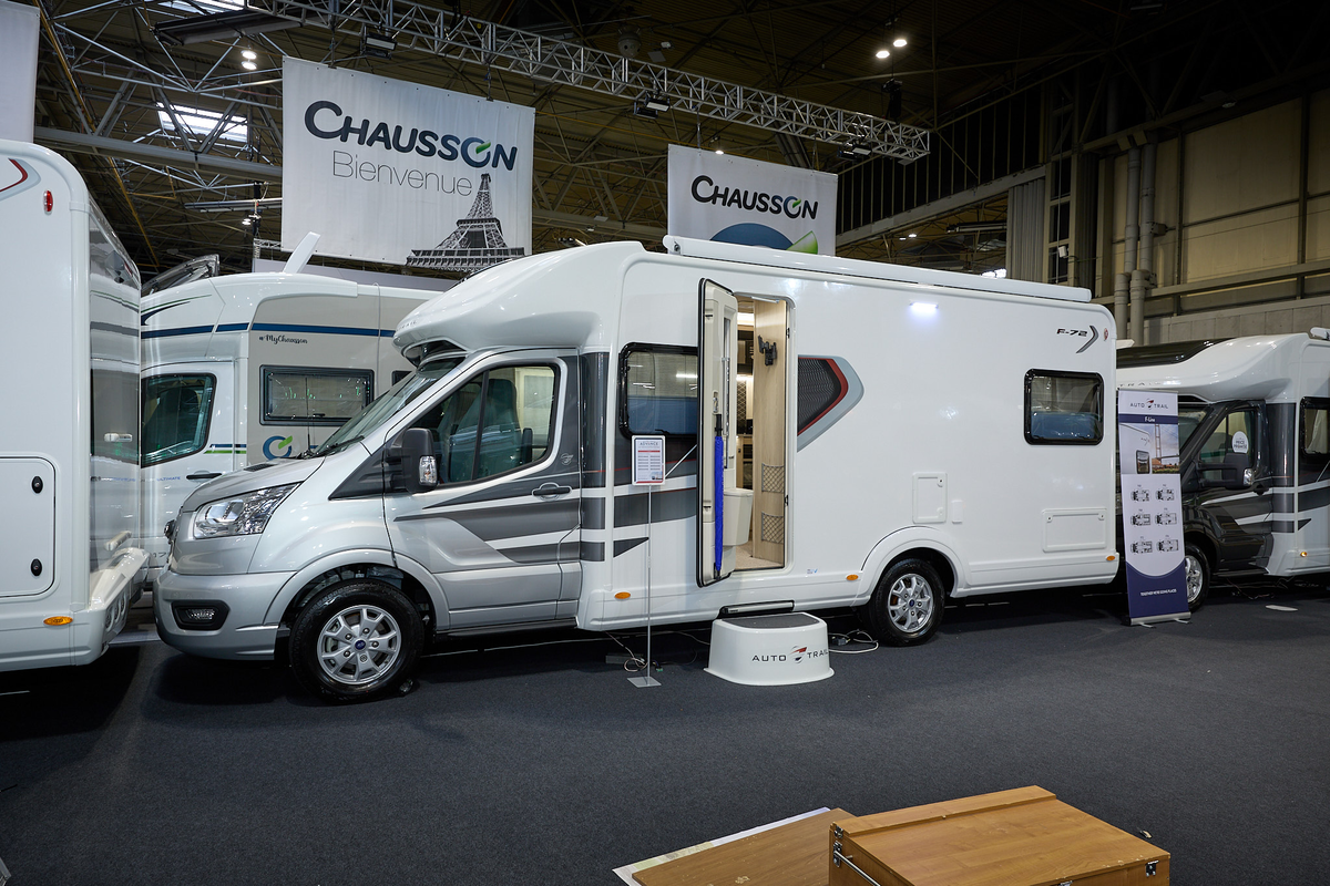 Auto-Trail F-Line F72's exterior is white with a silver cab.  There are grey and silver decals.  The entrance door is open revealing the lounge and there is a white step to gain easy access.  There is a roller banner to the rear.