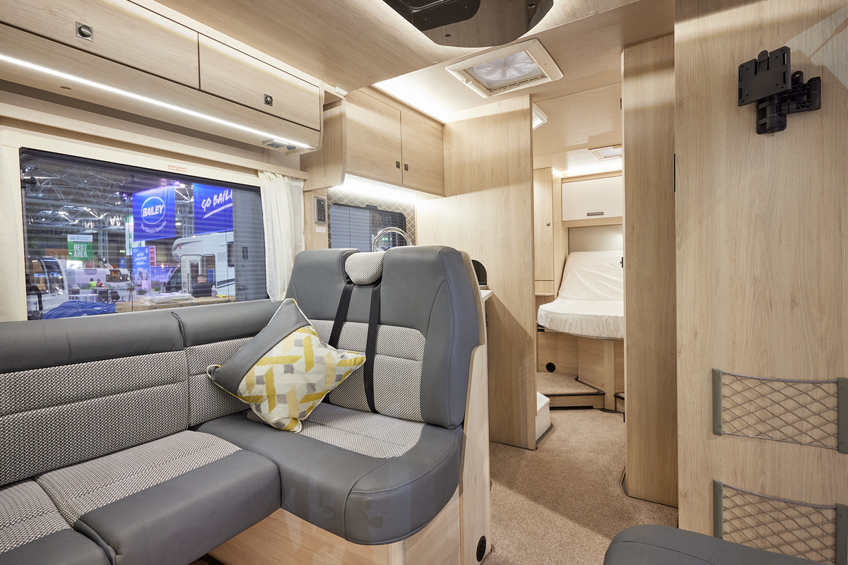 Auto-Trail F-Line F74 has two tone upholstery, with pale wooden furniture.  The floor has beige carpet.  To the rear is a fixed bed which is designed to lift the mattress at the top.  