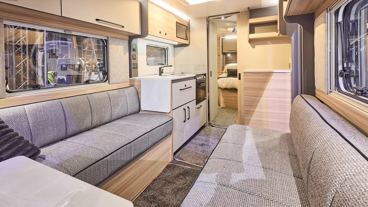 Interior of the Bailey Phoenix Black 640 with grey sofas and wood accents, large windows and two skylights will let natural light flood in.  To the rear the bedroom door is open. 