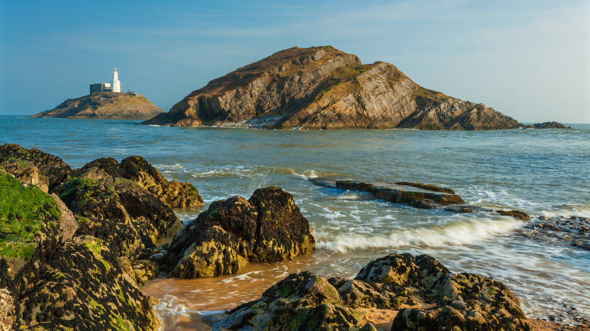 Rocks and a lighthouse in the sea on the coast of Swansea in Wales.