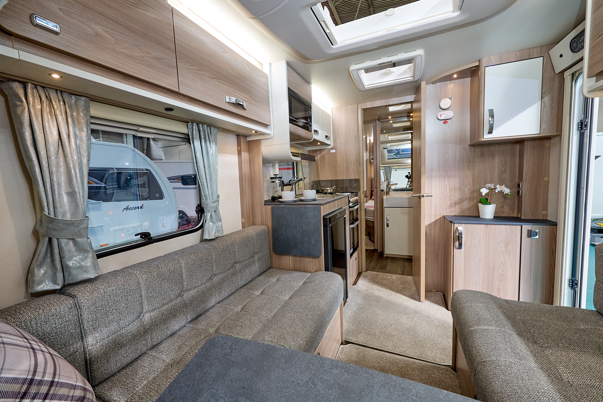Swift Sprite Major 4 EB's interior has wooden furniture with beige upholstery and carpet.  It has dark grey work surface and table top. The bedroom is to the rear.  The skylight is open.