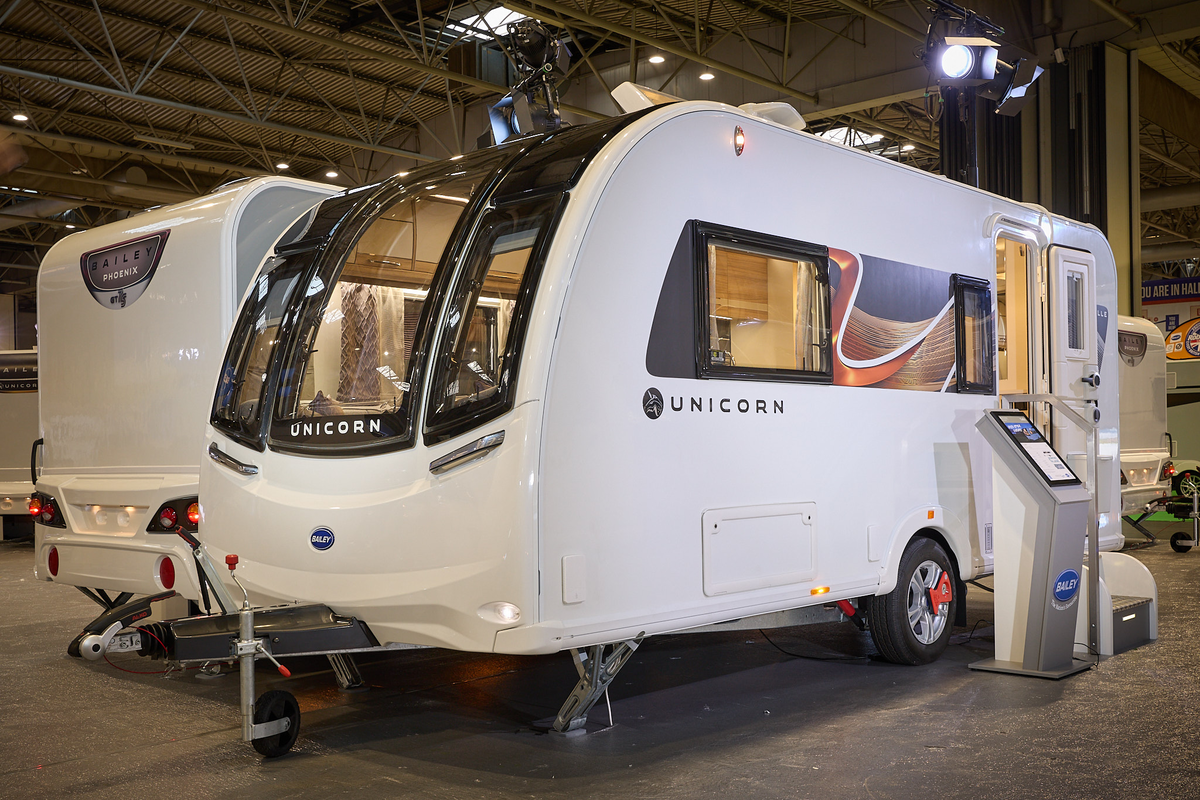 Bailey Unicorn Madrid exterior’s white with a large front window.  The entrance door is open and there are fixed metal steps into its interior.  There is an interactive stand next to the steps.