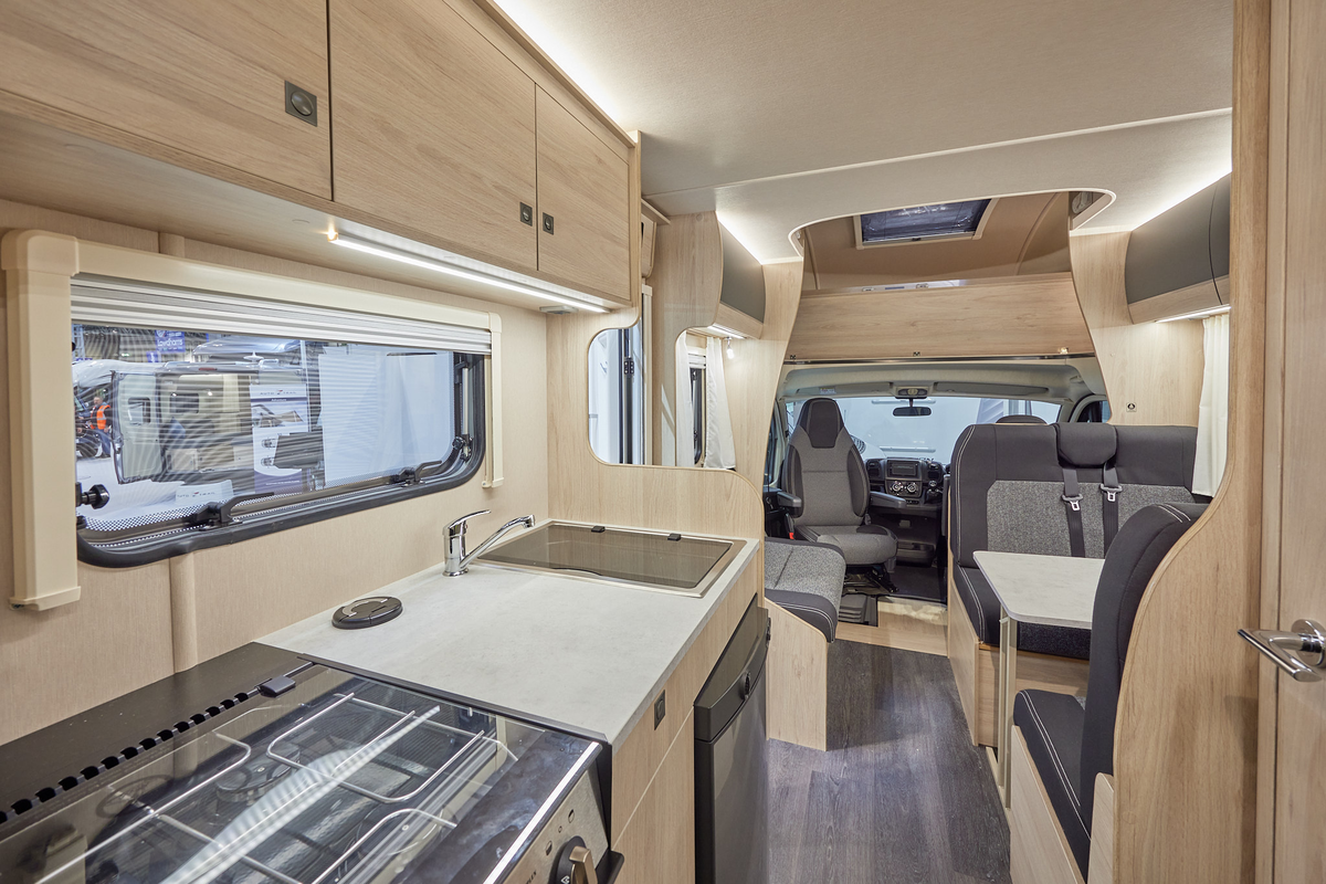 Auto-Trail Expedition C72 has two tone upholstery, with pale wooden furniture.  A hob, with a fridge underneath and a separate oven is in the kitchen.  The floor is dark wood.