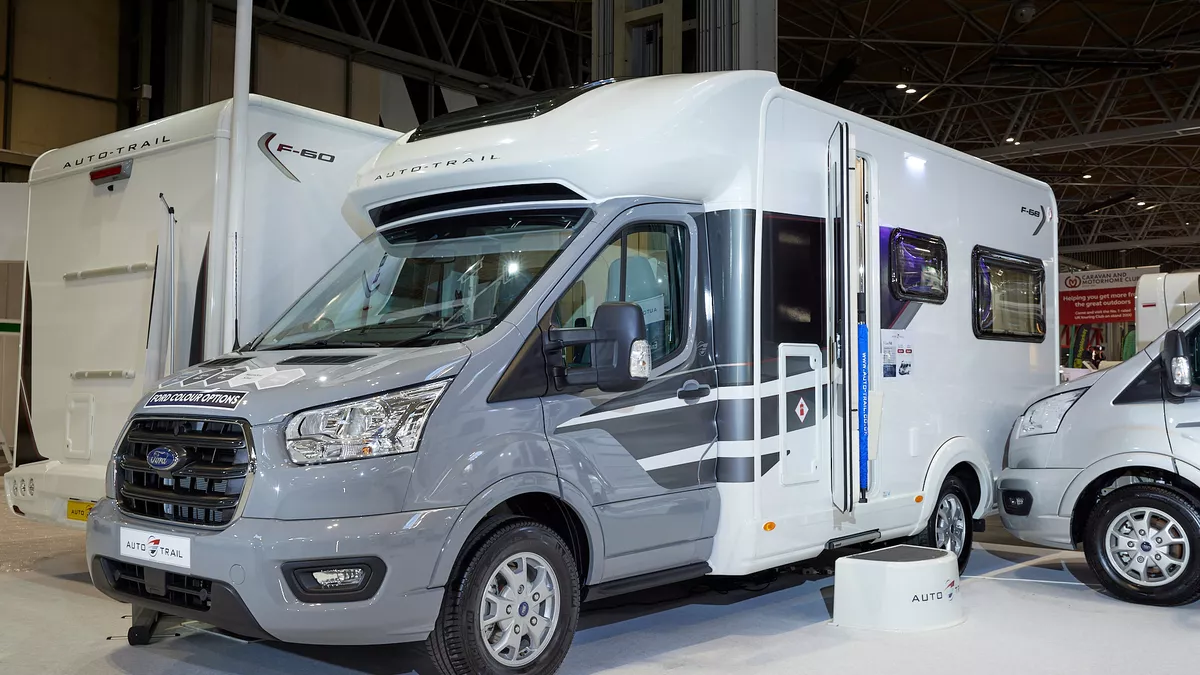 Auto-Trail F-Line F68 exterior, the motorhome has a grey cab with a white body, the habitation door is open showing into the interior, with a step to gain easy access.  There is a blue Auto-Trail umbrella in the door.