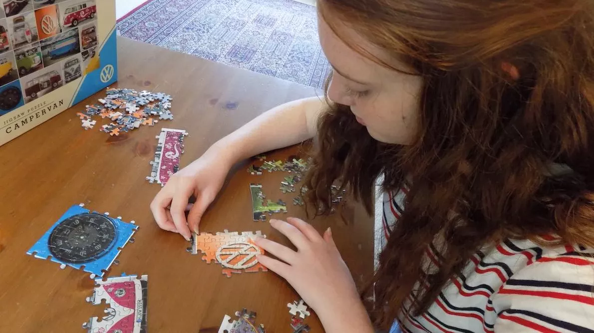 A girl pieces together a jigsaw of several campervans