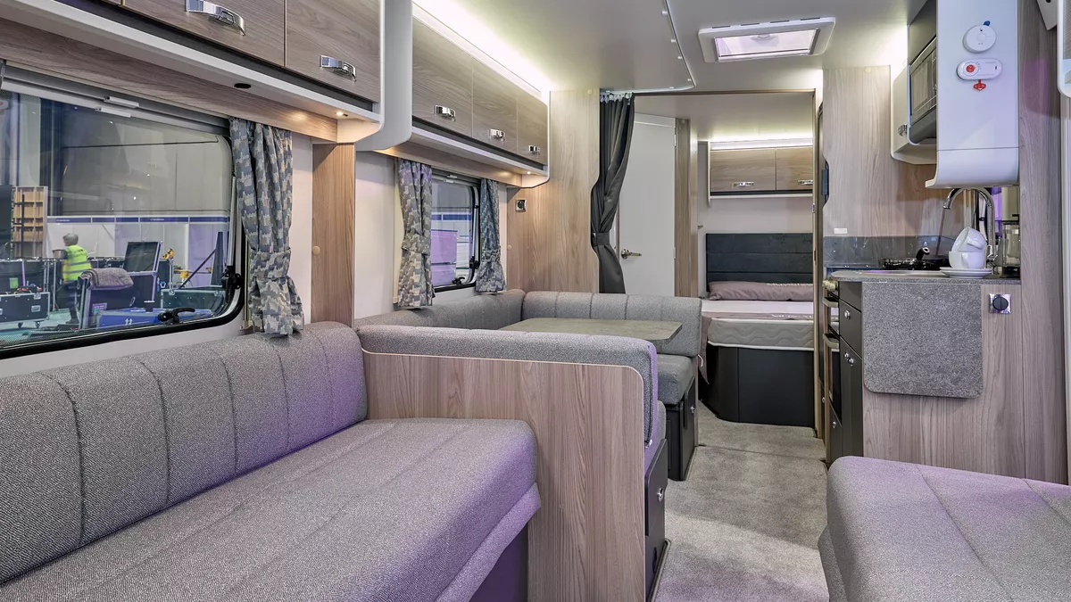 Swift Sprite Exclusive Quattro FB’s interior has a grey U shaped sofas with wooden furniture, there is a dinette opposite the kitchen unit.  The rear door is open revealing the fixed island bed.  