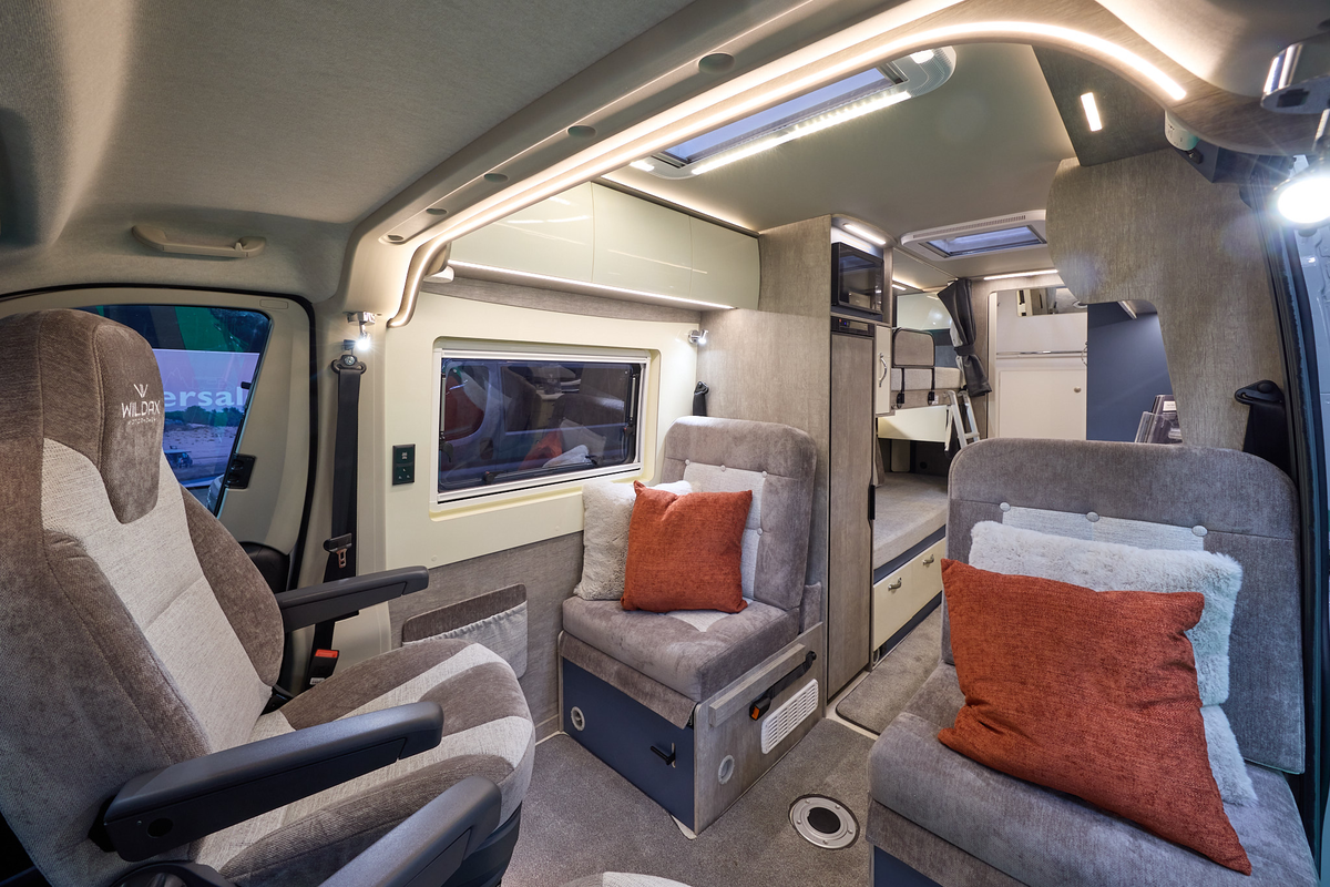 WildAx Motorhomes Solaris XL has brown and cream upholstery with two cushions on each passenger seat.  It has beige carpet.  To the rear there are fixed bunks with a silver ladder.