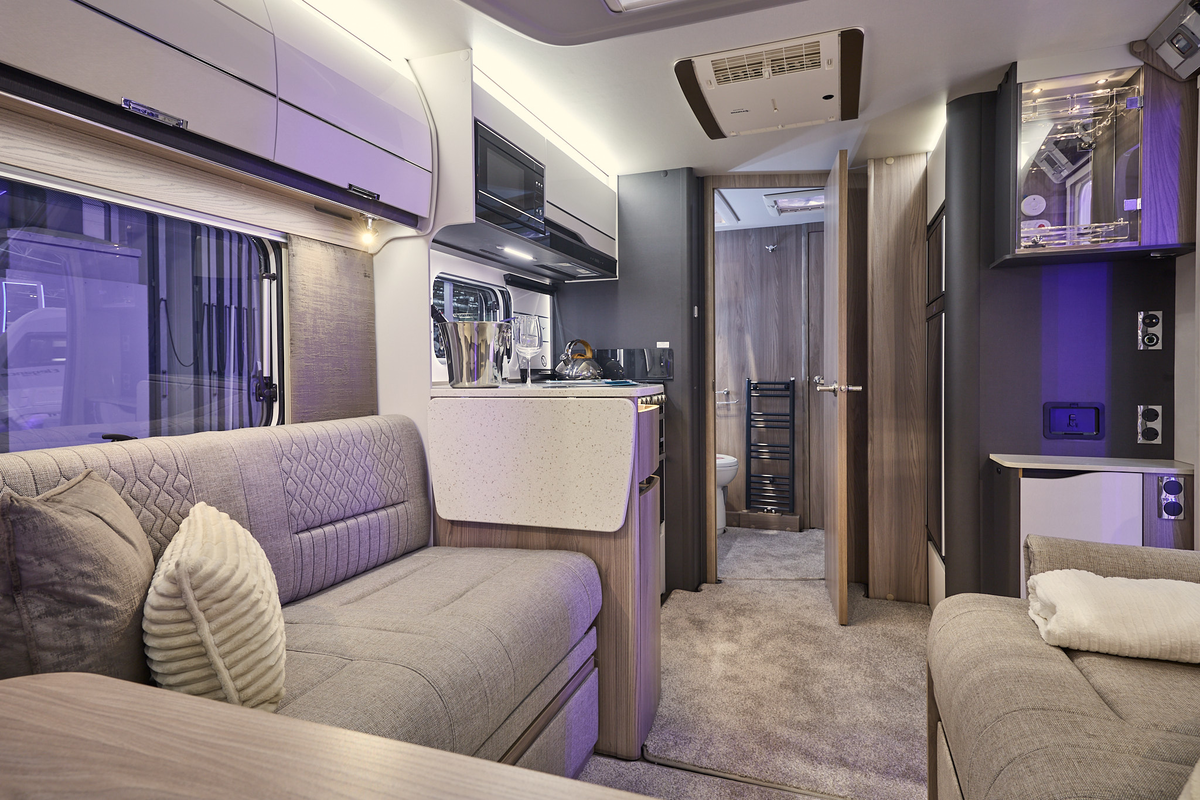 Swift Elegance Grande 835’s interior has wooden units with beige upholstery which has embossed patterns.  The rear door is open revealing the washroom