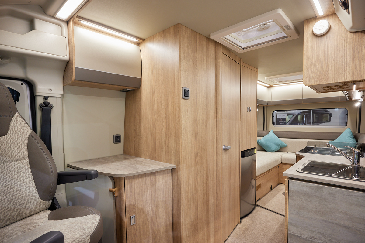 Auto-Trail V-Line 635 Sport has cream upholstery, with wooden furniture.  The floor has beige carpet.  The overhead lockers are cream.  The kitchen has a square sink and a flap to extend kitchen work surface.  The vehicle has a rear lounge.